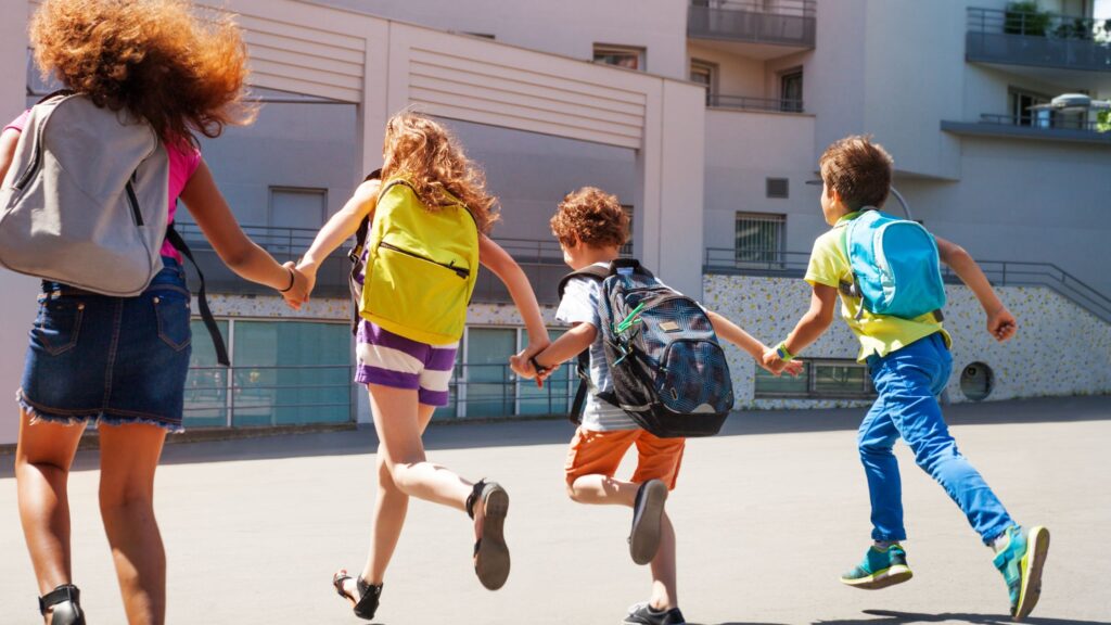 Kids holding hands and running with backpacks